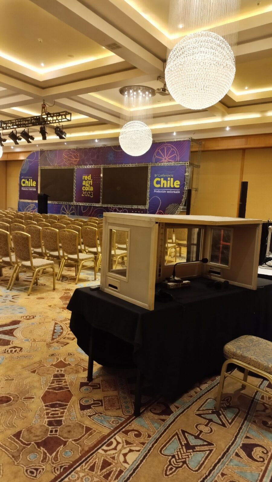 Cabina de traducción simultánea de sobremesa con consola y micrófono, instalada al fondo del salón frente al escenario de la conferencia