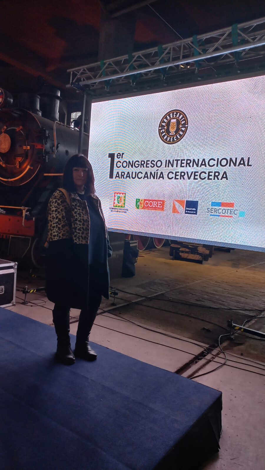 Pantalla LED con el nombre del 1er Congreso Internacional Araucanía Cervecera, junto a una locomotora a vapor del museo ferroviario