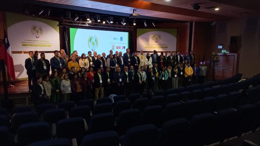 Fotografía oficial de las delegaciones sobre el escenario, con el pendón de la IV Cumbre Mundial de las Regiones y la bandera de Chile