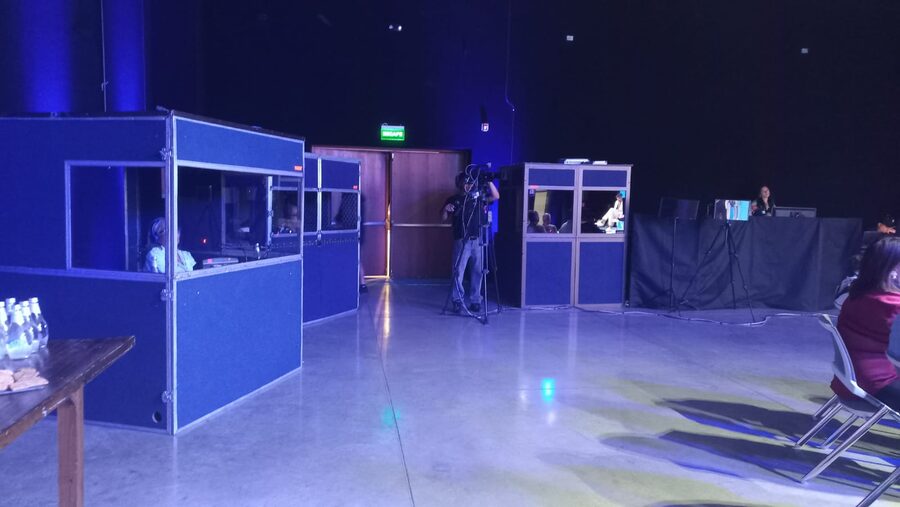 Dos cabinas de interpretación simultánea con los intérpretes trabajando dentro, y un camarógrafo grabando la sesión